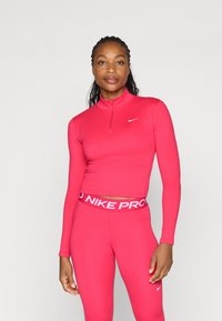 Fittet lyserød atletisk top med halv-zip krave og lange ærmer, parret med matchende høj talje leggings med en hvid mærkevare elastik.
