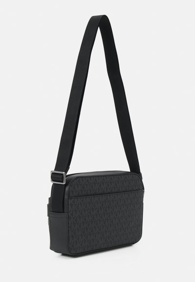 Sac à bandoulière noir en tissu texturé avec un motif logo répété subtil, fermeture éclair et sangle réglable.