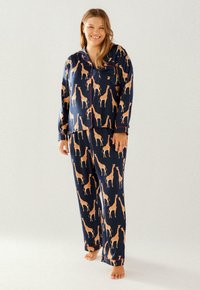 Navy pajama set with orange giraffe print. Features button-up top and elastic waistband pants. Soft fabric with contrasting trim accents.