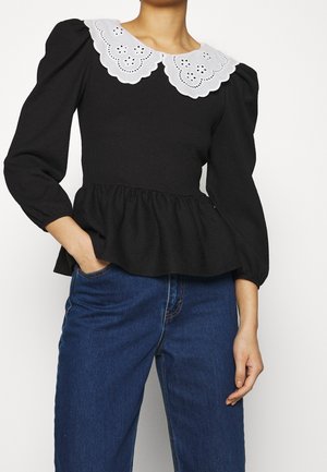 Sort peplum-top med lange puffærmer og en hvid scalloped krave med udskæringer. Stoffet ser tekstureret og let ud.