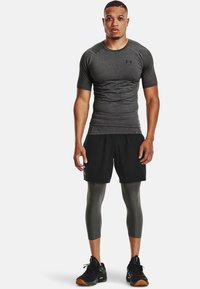 Shorts de sport noirs, t-shirt ajusté gris et leggings de compression gris. Baskets noires avec semelles en caoutchouc. Tissus lisses, design minimal.