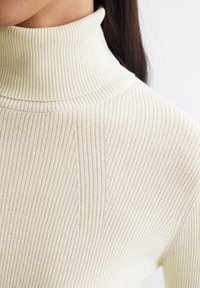 Helle beigefarbene, gerippte Rollkragensweater mit einem eng anliegenden hohen Kragen und dezenten Nahtdetails an der Vorderseite und den Schultern.