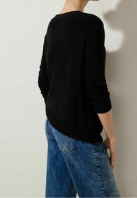 Black knit sweater with a boat neckline, ribbed cuffs, and a slightly curved hem, paired with light blue denim jeans.