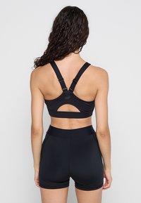 Czarny stanik sportowy z szerokimi ramiączkami, szczegółem w formie wycięcia na plecach oraz logo. Połączony z pasującymi czarnymi szortami z wysokim stanem o gładkiej fakturze.