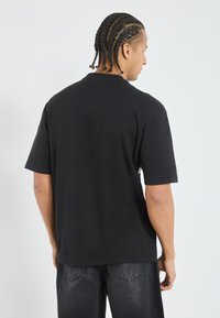 Svart bomulls t-shirt med avslappnad passform, korta ärmar och rundad halsringning, sedd bakifrån. Slät textur, minimalistisk design.