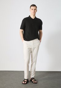 Polo negro de manga corta, pantalones beige ajustados y sandalias negras. Tejido suave, corte relajado y detalles mínimos en los botones.