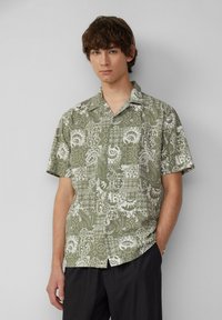 Camicia a maniche corte con bottoni di colore verde oliva, caratterizzata da un motivo floreale e geometrico bianco, dotata di colletto camp e vestibilità rilassata.