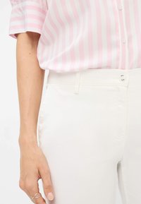 Roze en witte gestreepte blouse met korte mouwen, gecombineerd met witte strakke broek. De blouse heeft knopen en een subtiele glans; de broek heeft een platte voorkant.