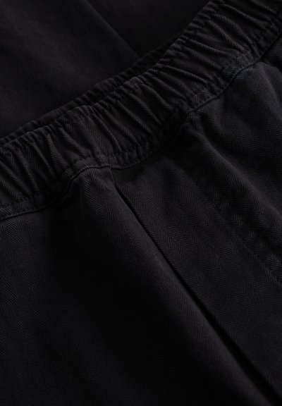 Tissu noir à motif chevrons, avec une ceinture élastique et une texture lisse. Vue en gros plan mettant en valeur les détails de la couture.