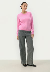 Roze trui met lange mouwen gecombineerd met grijs gestreepte wijdpantalon. De outfit heeft een zachte textuur en een ontspannen pasvorm. Zwarte schoenen maken de look af.