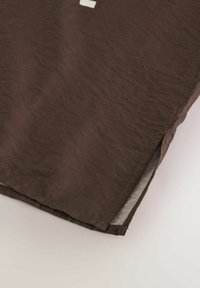 Tela marrón texturizada con una superficie ligeramente arrugada. Cuenta con una abertura lateral y un forro interior de contraste. Diseño simple y minimalista.