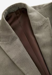 Hellgrauer Cordblazer mit strukturiertem Äußeren, braunem Satin-Futter und Spitzlapellen. Verfügt über eine detaillierte Naht am Kragen.