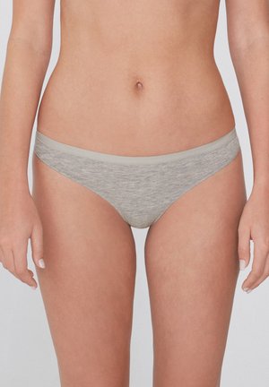 Mujer que lleva ropa interior bikini de algodón lisa de color gris claro, mostrada desde la mitad del torso hasta la parte superior de los muslos sobre un fondo liso.