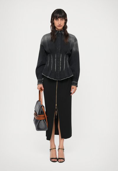 Czarna koszula dżinsowa o dopasowanym kroju, z lekkim wyblaknięciem, z detalami zamka błyskawicznego, w połączeniu z czarną spódnicą z przednim zamkiem i rozcięciem, nosząc szary plecak.