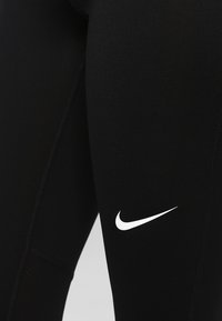 Leggings de sport noirs avec une texture lisse, ornés d'un logo Nike blanc sur le côté et d'une couture contrastée le long des coutures.