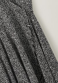 Tissu noir avec un petit imprimé floral blanc et une couture diagonale visible avec des boutons assortis le long de la jupe.