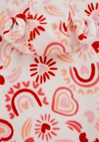 Tela de forro polar con un fondo color crema y patrones de corazones rojos y rosas, arcoíris y destellos solares. Textura suave con bordes enrollados.