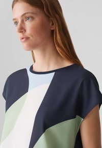Top multicolore in tessuto morbido con motivi geometrici in blu navy, azzurro, bianco e verde, con una vestibilità confortevole e scollo a girocollo.