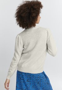 Suéter de punto gris claro con dobladillo acanalado, hombros ligeramente abullonados y un escote redondo, combinado con una falda de estampado de leopardo azul.
