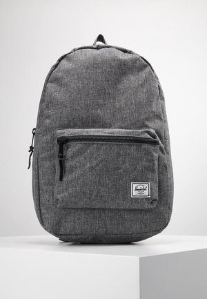 Sac à dos en tissu gris avec poche avant zippée, tirettes de fermeture éclair noires et une petite étiquette de marque blanche dans le coin inférieur droit.