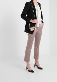 Blazer nero, camicetta bianca con cravattino, pantaloni beige e bordeaux con motivo, décolleté nere con punta e una piccola borsa a tracolla decorata.