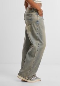 Light blue, high-waisted wide-leg jeans with a faded finish, featuring five pockets and stitching details, paired with gray sneakers.