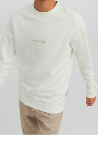 Ljuskrämfärgad sweatshirt med rund hals, ribbade ärmmuddar och fåll. Har en subtil logotyp i beige på framsidan. Mjuk tyg och avslappnad passform.