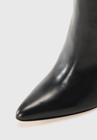 Stivaletto alla caviglia in pelle nera con punta affilata, texture liscia e design minimalista. Presenta un tacco sottile e una silhouette elegante.