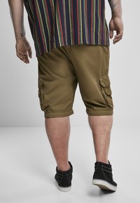 Olive green cargo šortky s bočnými vreckami, zrolovanými manžetami a ľahkým materiálom. Nosia sa s čiernymi teniskami po členky.