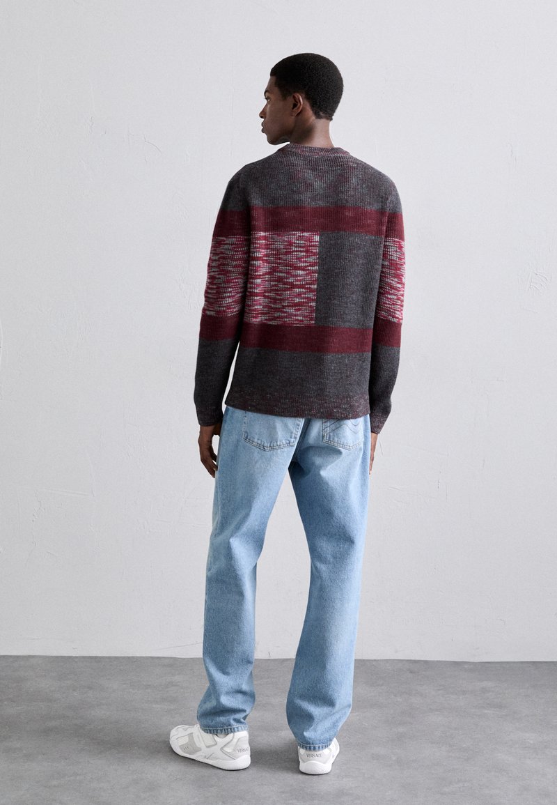 Gray and maroon patterned sweater with a round neck, paired with light blue denim jeans and white sneakers, viewed from the back.