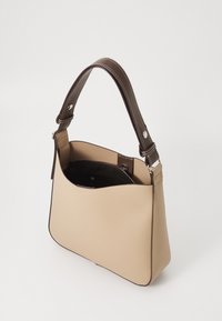 Beige läderhandväska med en strukturerad form och brunt läderrem. Har en blixtlåsförsedd innerficka, kontrasterande sömmar och en slät yta.