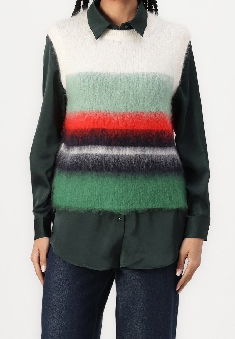 Sweter bez rękawów w zielone, czerwone i granatowe paski, noszony na ciemnozielonej koszuli z guzikami. Wykonany z miękkiego, puszystego materiału o luźnym kroju.