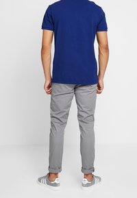 T-shirt blu navy a maniche corte, chinos a gamba stretta grigi chiaro e sneakers grigie con strisce bianche. Design semplice e aderente, con maniche arrotolate.