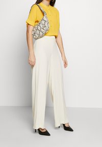 Camicia gialla con bottoni, pantaloni larghi crema, tacchi a punta neri e una borsa con stampa serpente a motivi. Design semplice e moderno.