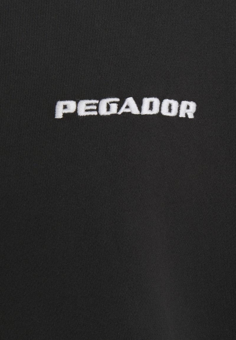 Camiseta de tela negra con el texto bordado en blanco "PEGADOR" centrado en el pecho. Textura suave con un escote redondeado estándar.