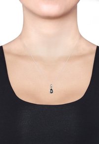 Halskette aus Sterlingsilber mit einem tropfenförmigen schwarzen Anhänger, der an einer zarten Kette hängt, vor einem schwarzen Oberteil.