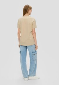 Beige T-shirt met korte mouwen en een ronde zoom, gecombineerd met lichtblauwe cargobroek met meerdere zakken en witte sneakers.