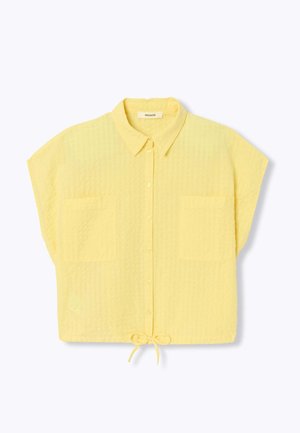 Chemise jaune à manches courtes avec deux poches avant, col et lien à l'ourlet, posée à plat sur fond blanc.