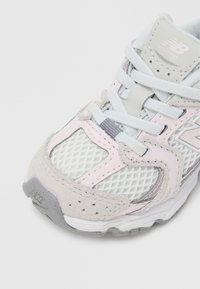 Ελαφρύ αθλητικό παπούτσι με δίχτυ στον επάνω μέρος σε γκρι και παστέλ ροζ, με μαξιλαρωμένη σόλα και λογότυπο στη γλώσσα.