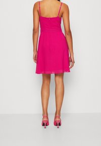 Fuksjowa sukienka w stylu A z regulowanymi ramiączkami, zamek z tyłu i zwiewnym dołem. Połączona z dopasowanymi różowymi szpilkami z cienkim obcasem.