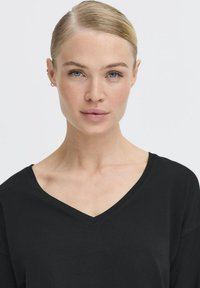 Schwarzes V-Ausschnitt-Shirt aus weichem Stoff, mit lockerem Schnitt und kurzen Ärmeln. Glatte Textur mit einfachem Design und ohne sichtbare Muster.