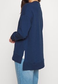 Felpa blu navy con scollatura rotonda, spalle scese e spacchi laterali; realizzata in tessuto morbido con vestibilità comoda.