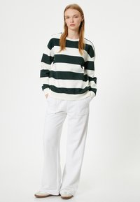 Felpa a righe verdi e bianche con maniche lunghe, abbinata a pantaloni bianchi a gamba larga e scarpe beige. Tessuto morbido con vestibilità rilassata.