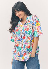 Buntes Kurzarmhemd mit tropischem Blumen- und Tierdruck auf weißem Hintergrund, mit lockerem Schnitt und Knopfverschluss.