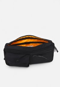 Sac zippé noir avec un intérieur orange, doté d'une poche extérieure et d'un matériau textile lisse. Design compact pour une utilisation polyvalente.