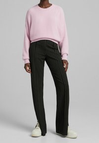 Pull rose clair texturé avec un col rond ; associé à un pantalon long rayé noir. Des baskets blanches complètent la tenue.
