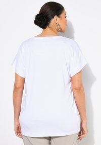 Top blanco de manga corta hecho de algodón suave, con un corte holgado y dobladillo redondeado. La parte posterior presenta una textura suave con costuras mínimas.