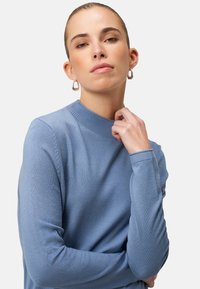 Light blue, knitted sweater with a ribbed neckline and long sleeves, featuring a smooth texture and fitted design.