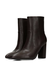 Bottines en cuir marron avec une texture lisse, bout pointu et talon carré épais. Elles présentent de discrètes découpes latérales pour un enfilage facile.