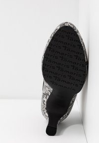 Chaussure à talon haut à bout pointu avec tige imprimée serpent et semelle noire présentant un motif répété du texte "tamaris".
